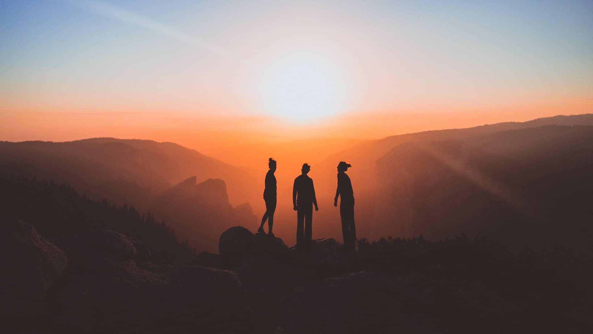 Three people watching the sun rise on a mountain top
